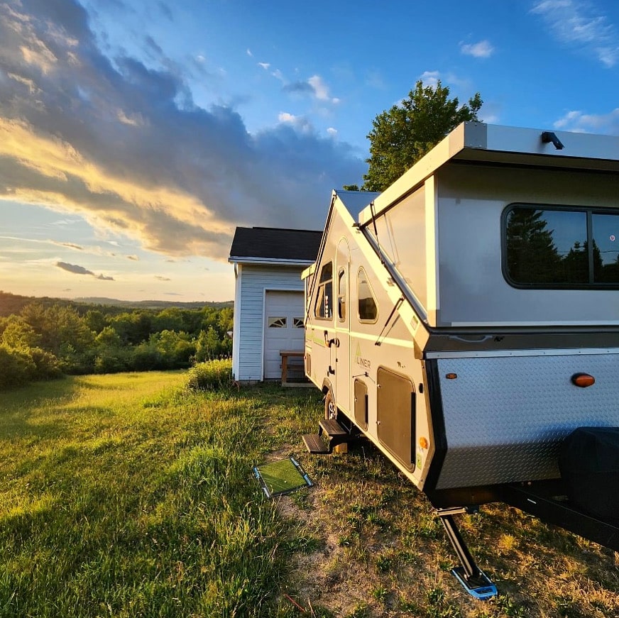 A white camper parked in the grass near a house.