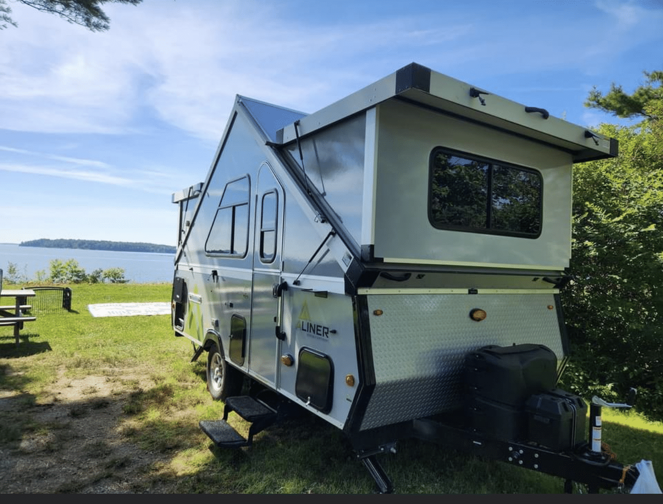 A camper trailer parked on the grass near water.