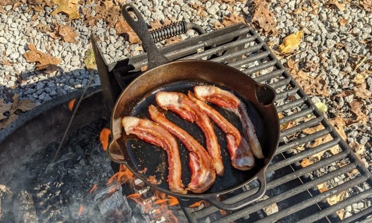First time campers learning how to cook bacon over a campfire in a skillet.