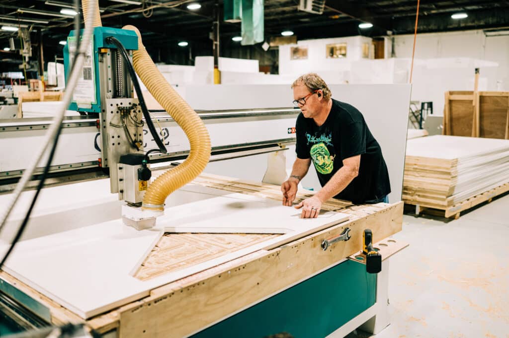 Man operating CNC machine to manufacture a sustainable A-frame camper.