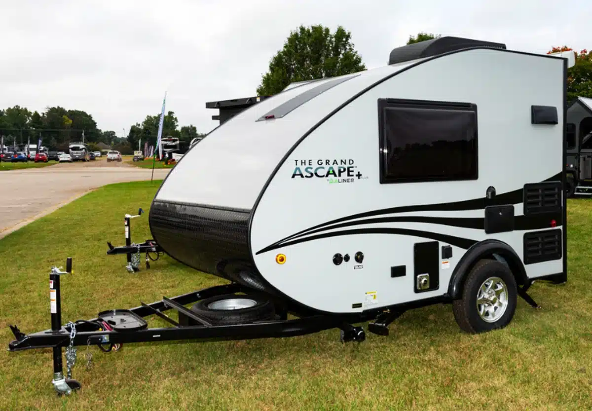 A parked travel trailer with "the grand ascape" branding on a grassy area.