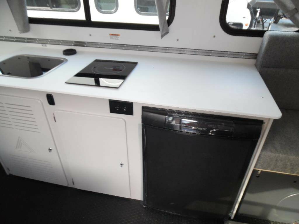 Compact kitchenette inside a camper van with a sink, stove, and refrigerator.
