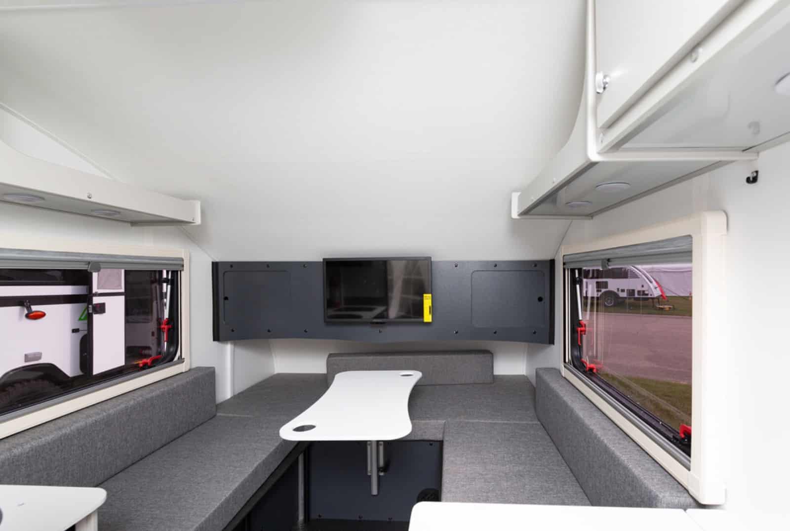 Interior of a modern camper van with bench seating and a central table, equipped with storage cabinets.