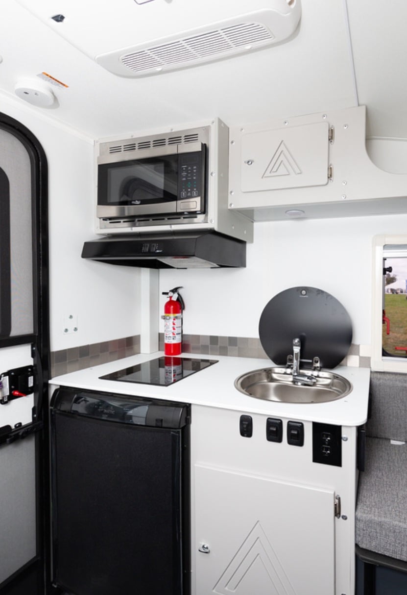 Compact camper van kitchenette with microwave, sink, and refrigerator.