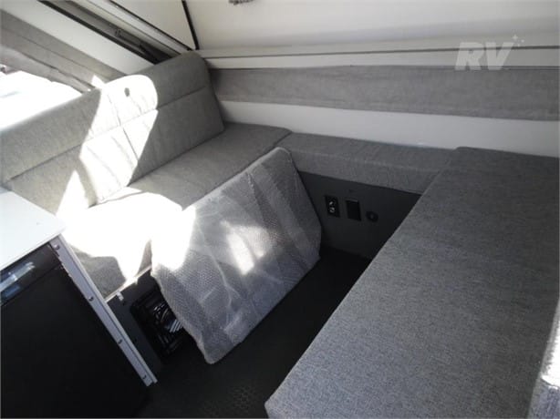 Interior of a modern rv showing a seating area with grey upholstery and a bench that doubles as a sleeping space.